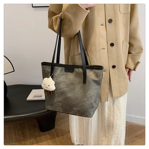 Detail of grey matte tote bag with black strap and plush cloud charm on female model