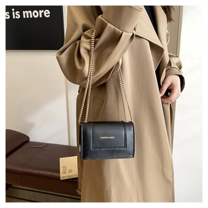 Close-up of black leather crossbody bag with gold chain strap worn by a model