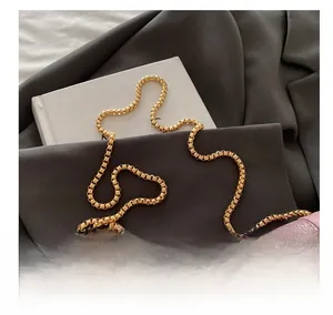 Détail de la bandoulière chaîne dorée sur un sac pailleté rose posé sur un blazer gris