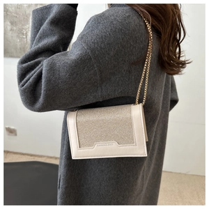 Détail du sac beige à chaîne avec texture scintillante porté sur un manteau en laine