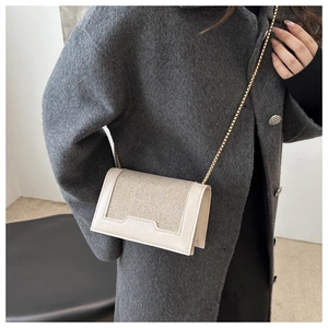 Détail du sac bandoulière crème avec chaîne dorée et finition pailletée sur manteau