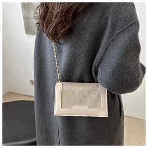 Détail du sac à bandoulière crème avec texture verticale fine et chaîne dorée sur manteau