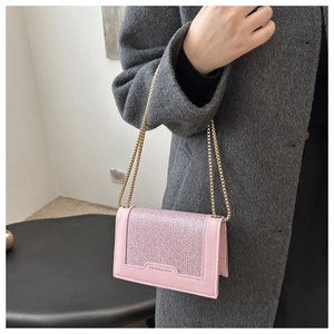 Sac à bandoulière rose pailleté avec chaîne dorée porté sur un manteau en laine