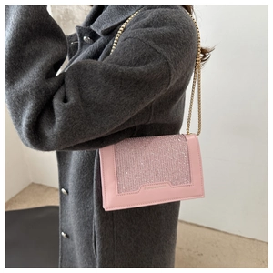 Détail du sac bandoulière rose à paillettes avec chaîne dorée sur manteau gris