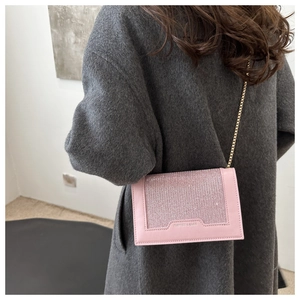 Détail du sac à bandoulière rose à paillettes avec chaîne dorée sur manteau gris