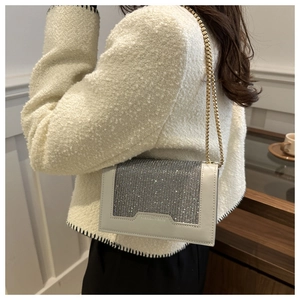 Détail d'un sac à bandoulière crème avec rabat en strass étincelants et chaîne dorée chic