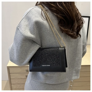 Détail du sac bandoulière à paillettes noires avec chaîne dorée et badge métallique