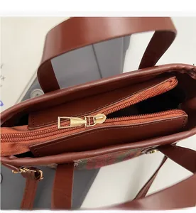 Detailed close-up of smooth metal zipper and plaid wool texture on brown leather bag