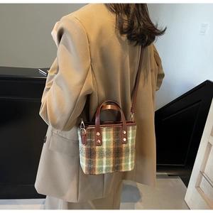Close-up of green and brown plaid wool handbag showing leather strap and gold hardware
