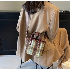 Detail of plaid tweed bucket bag with brown leather handles and gold metal rivets