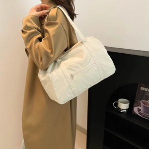 Large off-white nylon tote bag with front zipper pocket shown on a model in trench coat