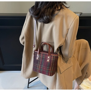 Detail of vintage red plaid woolen tote with brown leather handles and gold rivet accents