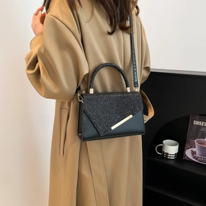 Sac à main noir élégant avec panneau pailleté et barre dorée sur modèle en trench
