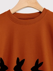 Detail of caramel crewneck sweatshirt featuring black rabbit silhouette print and ribbed collar