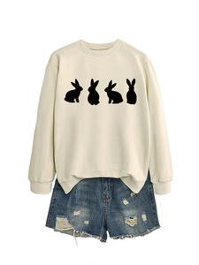 Flat lay of a beige crewneck sweatshirt with black rabbit silhouettes and ripped denim shorts