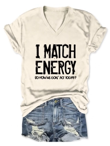 Close-up of beige V-neck T-shirt with 'I MATCH ENERGY' text and distressed denim shorts