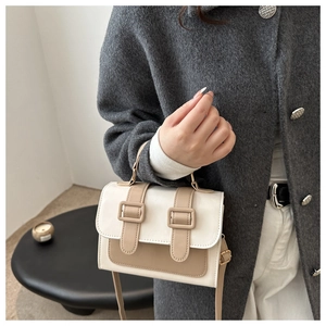 Detail of contrast color square handbag with decorative straps and short top handle