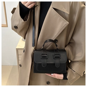 Detail of a structured black crossbody bag with flap and dual buckle accents on a model