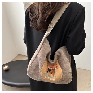 Detail of a brown corduroy underarm bag featuring a cute cat patch and shoulder strap