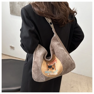 Detailed close-up of brown corduroy shoulder bag featuring cute cat embroidery and text