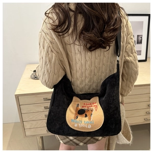 Detail of cute cat embroidery on a black corduroy shoulder bag shown in home setting