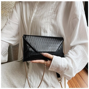 Détail d'une pochette noire à texture ondulée avec bandoulière en chaîne dorée