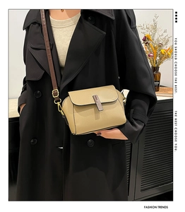 Detail of beige litchi grain leather crossbody bag with dark brown strap on black coat