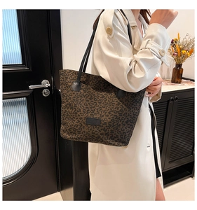 Detail of dark leopard print tote bag worn with white trench coat in a stylish home setting