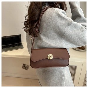 Detail of a brown leather shoulder bag featuring a golden spiral twist lock and knotted strap