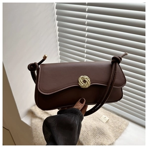 Detail of a brown leather shoulder bag featuring a gold circular buckle and knotted strap