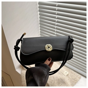 Detail of a matte black underarm bag featuring a golden knot clasp and thick rope strap