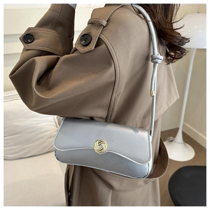 Detail of silver-grey small square bag with golden ring buckle worn over a brown coat