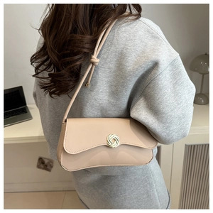 Close-up of beige shoulder bag featuring a golden circular weave buckle and knot strap detail