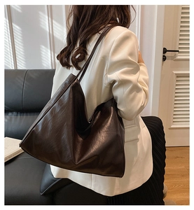 Detail view of a large brown faux leather tote bag worn as a shoulder underarm bag