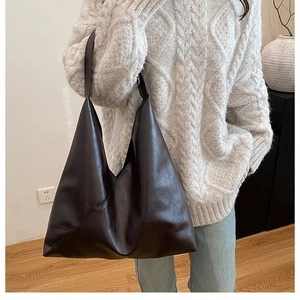 Large brown leather tote bag worn by model, showing spacious bucket shape and texture