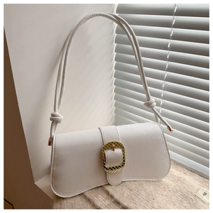 Close-up of white leather baguette bag with textured gold buckle on a beige rug