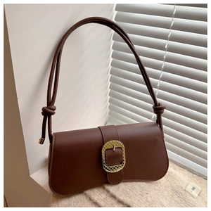 Close-up of brown leather bag with a large textured golden oval metal buckle and knot strap