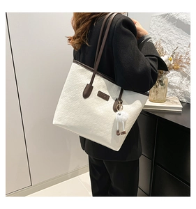 Detail of white embossed tote bag with brown trim and plush charm worn with black suit