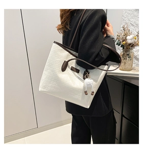 Detail of white embossed leather tote bag with brown handles and plush doll pendant