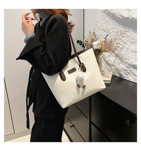 Detailed view of cream tote bag with letter embossing and plush ball charm accessory