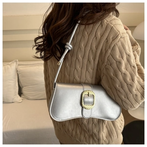 Close-up of silver baguette bag with gold buckle and twisted strap on shoulder