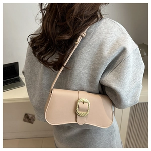 Close-up of beige baguette bag with gold buckle on a model in minimalist setting