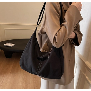 Grand sac hobo noir avec surpiqûres blanches porté sur une veste de costume kaki