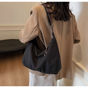 Détail d'un sac hobo en toile noire avec surpiqûres blanches et bandoulière marron