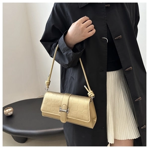 Detailed view of metallic gold crocodile embossed texture on shoulder bag with knot strap