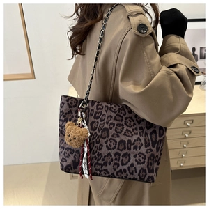 Detail of leopard print tote bag featuring chain strap and plush bear charm on model