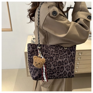 Detail of leopard print tote bag with gold chain strap and teddy bear charm on trench coat