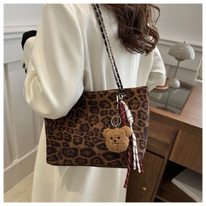 Detail of leopard print tote bag with chain strap and teddy bear charm worn by a model