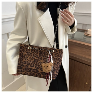 Detail of leopard print tote bag featuring a gold chain strap and plush bear charm accessory