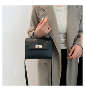 Detail of classic black cross-grain leather bag with gold metal rotary lock on gray coat